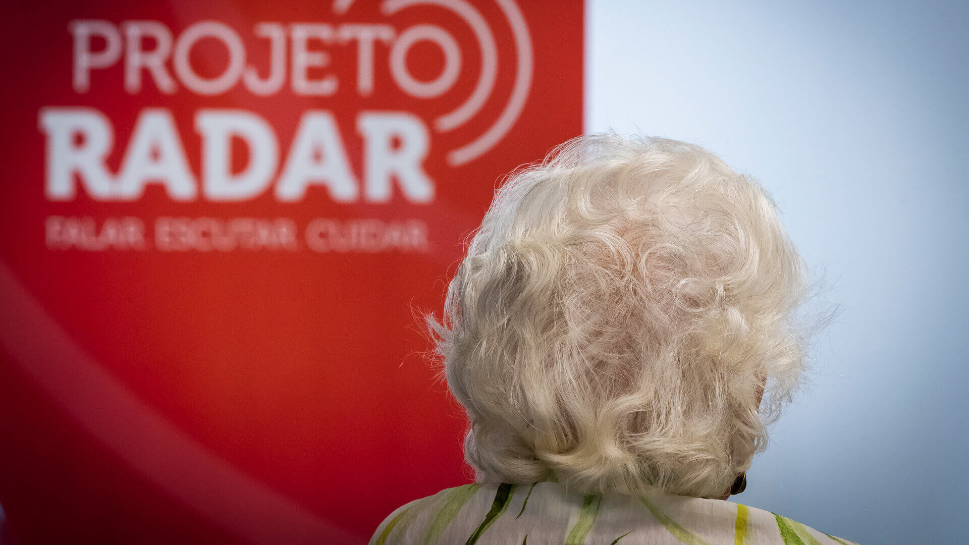 Senhora de costas com um cartaz do projeto radar no fundo