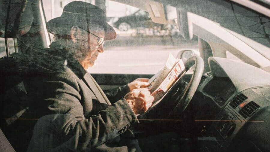 Senhor de idade dentro do carro a ler o jornal